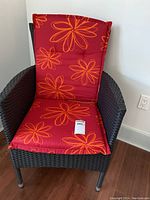 Front view of dark brown synthetic wicker patio chair with red and orange floral cushion.