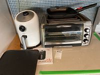 Overall view of lot showing white Dash air fryer, stainless steel toaster oven and multiple baking trays stacked on top
