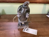 Three-quarter front view of soapstone carving depicting Inuit hunter wearing parka, holding bow and arrow, mounted on stone base with lot tag visible