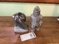 Photo showing both soap stone carvings on wooden surface: two seals and indigenous man figure