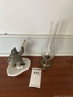 Photo showing soapstone Eskimo fishing figure and brass oil lamp on floor against baseboard