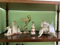 Shelf with marble bookends shaped as polar bears holding white crystal formations, ceramic candle holder with yellow and blue floral designs, sand sculpture bottle with layered sand art, and a white paper mache clown figurine.