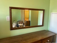 Full view of the rectangular mirror mounted above a wooden dresser against a green wall, showing the mirror size and condition of the frame.