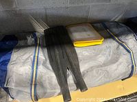 Gray nylon carrying bag with yellow and blue straps, two oar blades and plastic box on top