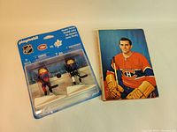 Playmobil NHL Rivalry Series #9013 figures in original blister card packaging with taped plastic cover alongside vintage Rocket Richard hockey biography book with dust jacket.