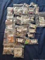 32 pieces of assorted costume jewelry individually sealed in plastic bags on a fabric surface.