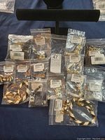 Photo of 15 pieces of assorted costume jewelry in separate plastic bags laid out on a surface with a black jewelry T-bar stand behind.