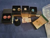Overview of four rings and three pairs of stud earrings displayed in individual boxes and on a ring stand