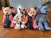 Four Ty Beanie Babies bears lined up showing overall lot contents: two Spangle bears with stars and stripes patterns, one light blue America bear with US flag patch, and one stars-pattern Glory bear.