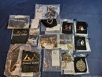 Full lot of 14 assorted Charles Albert jewelry pieces including rings, earrings, and pendants shown in original bags and packaging on dark cloth.