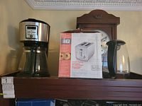 Coffee maker, white toaster with box, and transparent electric kettle on shelf