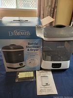 Photo showing the Dr. Browns Bottle Sterilizer and Dryer with box, instruction manual, and a filter pack on a table.