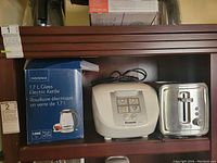 Insignia 1.7 L glass electric kettle in box, Panasonic rice maker and Black & Decker toaster inside wooden shelf