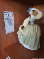 Porcelain Royal Doulton Buttercup figurine positioned on wooden shelf, visible from oblique side angle showing the bonnet and front of the dress.