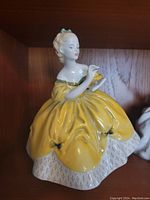 Front view of the Royal Doulton figurine depicting a woman in an elaborate yellow dress holding a fan.