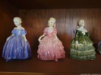 Front view of three Royal Doulton figurines Belle, Rose, Marie in purple, pink, and green dresses.