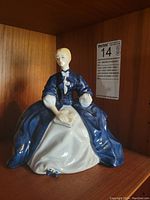 Front view of Royal Doulton Laurianne figurine, seated woman in blue and white dress with book on lap.