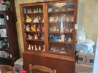 Front view of teakwood buffet and hutch showing sliding glass doors with shelves displaying figurines and other items. Lower section features two sliding wooden doors with recessed handles.