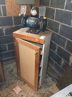 Front angled view showing the entire bench grinder mounted on the cabinet, cabinet door closed.