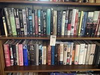 Wide view of two bookshelves filled with a mix of fiction and non-fiction hard and soft cover books, primarily historical and military themes.