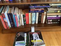 Photo showing assorted books on a wooden shelf including fiction, history, reference and nature books, with some titles visible like 'Dark Money', 'The Jungle Book', and others.
