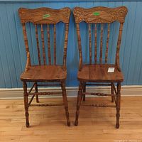 Two matching wooden chairs with carved backs in front of blue wall and wood floor