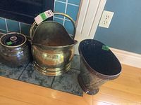 Three items on tile hearth: ceramic crock with lid, brass-look metal bucket with handle, and metal waste can.