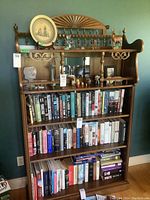 Full frontal view of a tall solid wood bookshelf with sunburst back panel and multiple shelves filled with books and some decorative items on the top shelf.