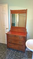 Front view of wooden dresser with mirror showing three drawers and scalloped top of mirror frame