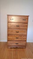 Frontal view of the wooden dresser showing all five drawers with metal handles and the scalloped base.