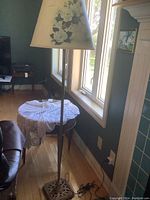Full view of brass floor lamp next to window, showing floral lampshade and base.