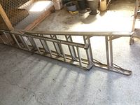 Aluminum multi-purpose ladder folded resting on ground showing rectangular and round tubular rungs and feet designed for stability.