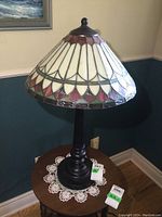 Full view of the stained glass table lamp on a wooden table showing off the entire base and shade.