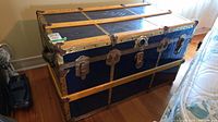 Full view of vintage steamer trunk showing blue metal panels, yellow wood strapping and brass hardware with lock insert.