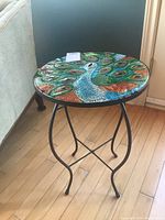 Full view of round table with colorful peacock glass top on black metal frame base showing the complete item.