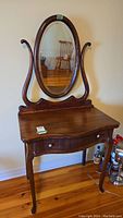 Full view of vintage wooden vanity with oval mirror and one drawer, showing curved legs and dark wood finish.