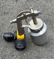Air spray gun with metal container and yellow-black pressure regulator with dial gauge showing pressure including bar and PSI readings