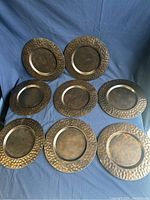 8 hammered copper trays displayed fully visible on a blue cloth background, showing top views and texture details.