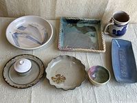 View of all 7 pottery pieces arranged on fabric background showing variety of shapes and glazes
