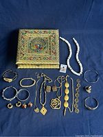 Full lot layout of women's jewelry pieces arranged next to decorative box on dark blue background.