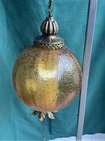 Wide shot of the mid century modern globe hanging lamp with amber glass globe and brass details, suspended against a blue background.