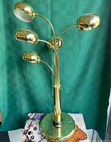 Front view of tiered brass lamp with five eyeball-style orb lamp heads, showing polished brass finish and curved stems.