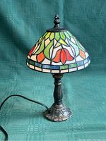 Mini portable lamp shown on green fabric background, stained glass colored shade and metal base visible.