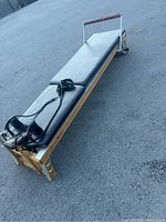 Full view of PilatesWorks reformer showing aluminum and wood frame with padded black bench and adjustable straps at foot end