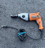 Ridgid R5010 1/2 inch hammer pulse drill laid on asphalt, showing full side view with coiled power cord.