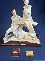 Front and side view of the signed G. Armani figurine showing the two characters and the wooden base with accompanying certificate and booklet.