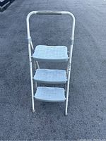 Front view of the white Werner step stool showing all three textured plastic steps and the handle with rubber grip.
