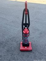 Front angled view of red Dirt Devil vacuum cleaner showing the base, dust container and hose setup.