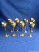 Front image showing all 8 vintage brass wine goblets arranged in rows against a blue fabric background.