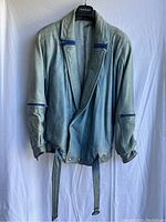 Front view of vintage Pegabo light blue leather jacket hanging against white backdrop. Shows full jacket with belt and blue zipper accents.